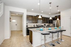A modern kitchen with dark cabinets, a large island with bar stools, and pendant lighting.