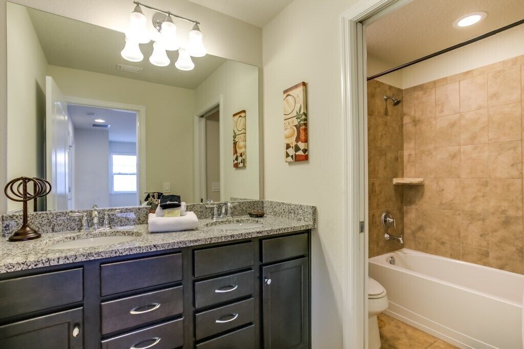 A bathroom with a granite countertop, dark cabinets, a white toilet, and a bathtub.