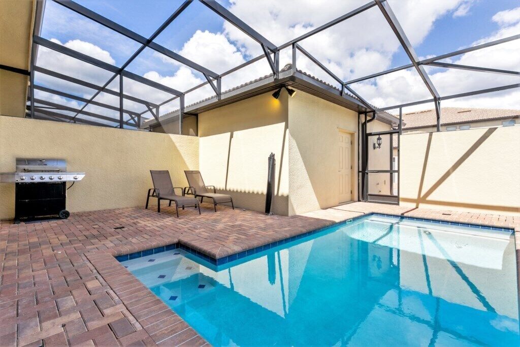 An indoor swimming pool with a glass ceiling, a barbecue grill, and lounge chairs.