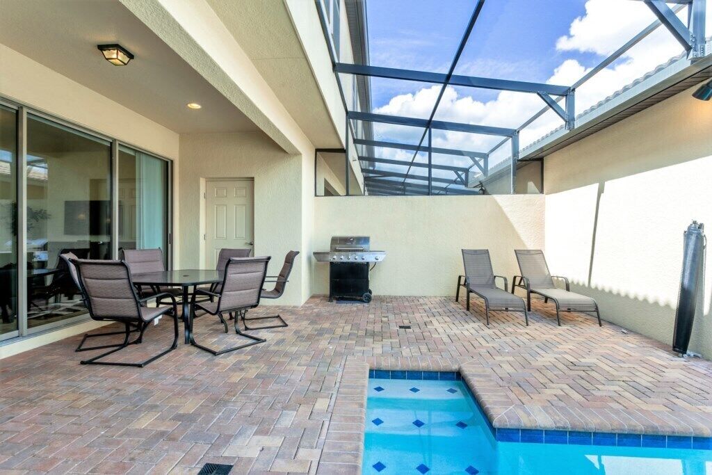 Um pátio externo com piscina, churrasqueira e áreas de estar.