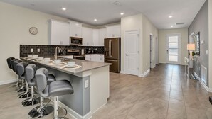 Uma cozinha moderna com ilha central, banquetas, eletrodomésticos de aço inoxidável e vista para a sala de estar.