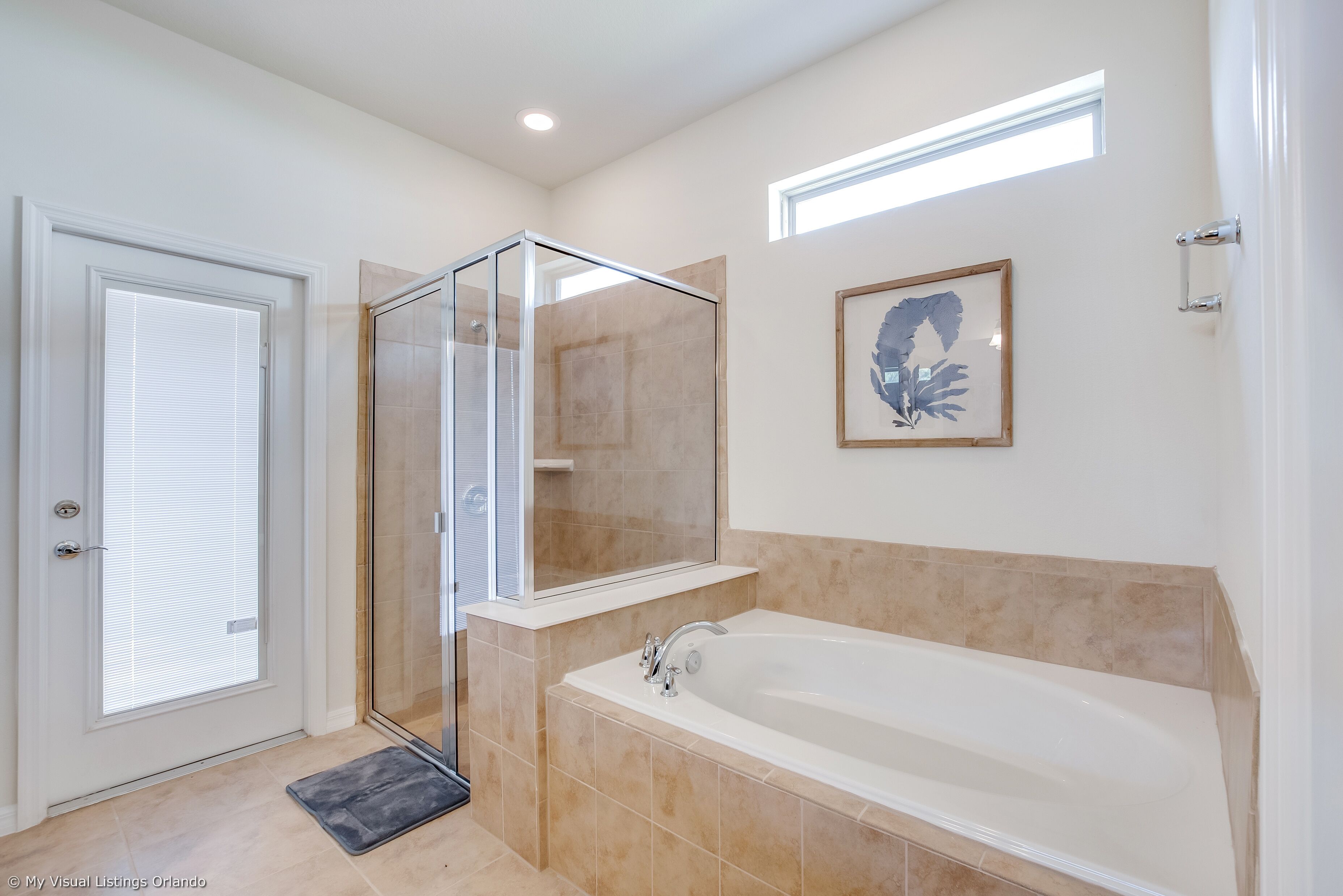 A modern bathroom with a glass shower enclosure, a large bathtub, and a framed artwork on the wall.