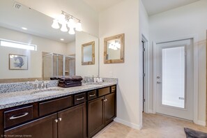 A bathroom with dark wooden cabinets, a granite countertop, a large mirror, and a door with a window. - 8805bengal (Kissimmee)