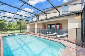 A swimming pool with a glass enclosure, surrounded by a patio area with outdoor furniture and a covered seating area. - 8805bengal (Kissimmee)