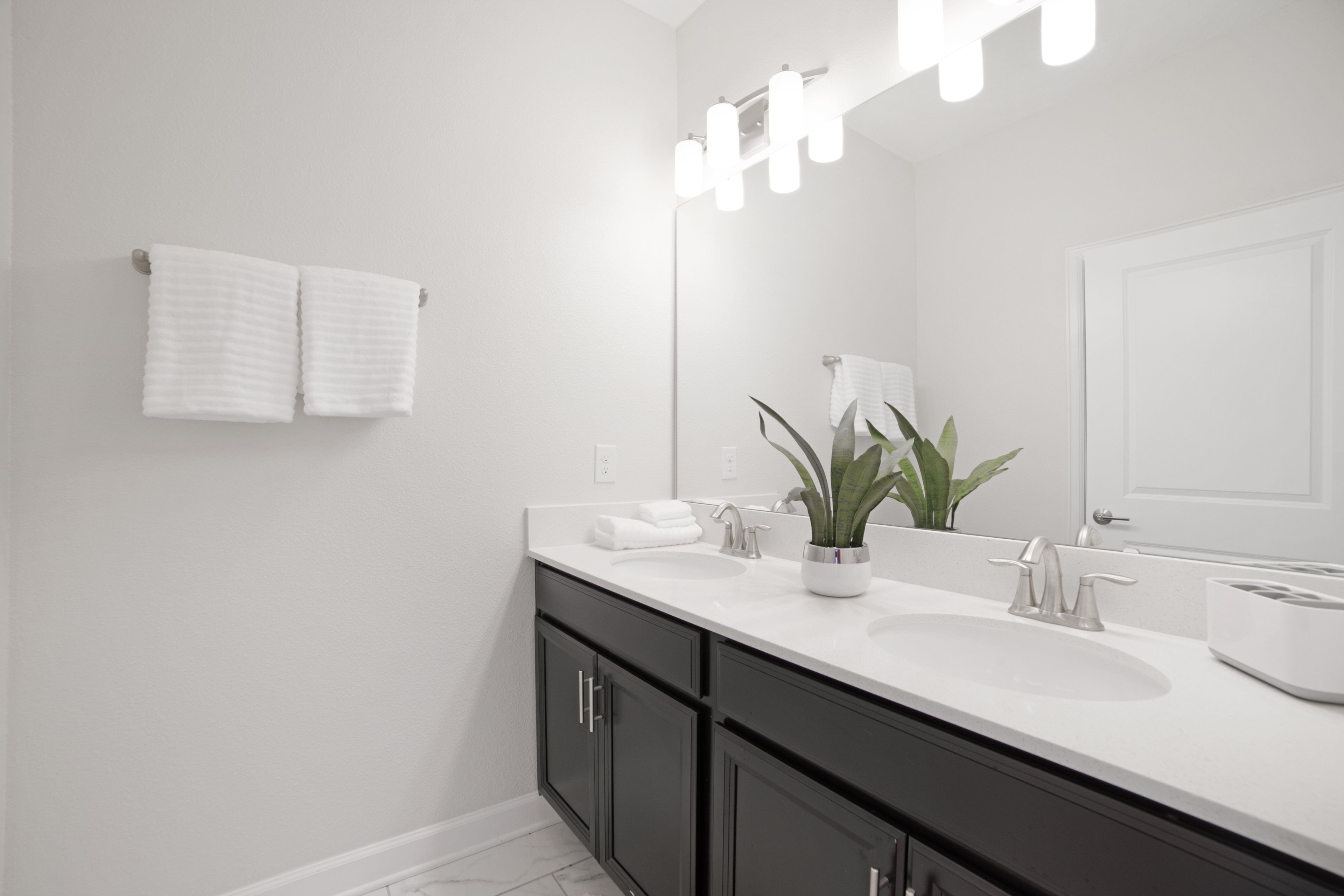 A modern bathroom with a white sink, dark cabinets, and a mirror with lights.