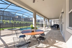 A covered patio with a pool, outdoor seating, and a view of a greenhouse.