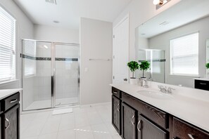 A modern bathroom with a glass shower enclosure, a large mirror, and dark wooden cabinets.