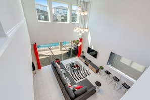A modern living room with a large sofa, a TV, and a pool view.