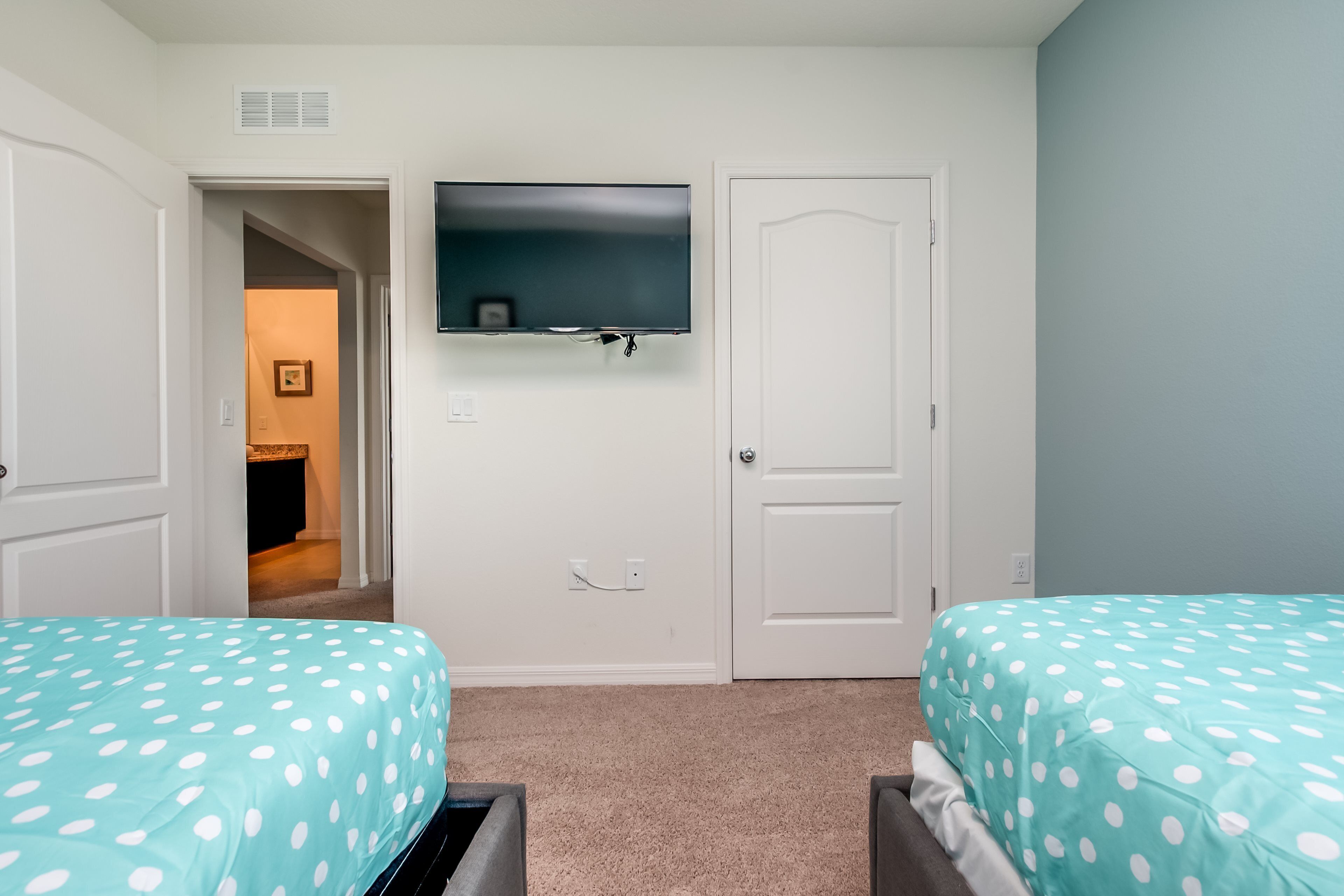 Une chambre avec deux lits, un téléviseur fixé au mur et une porte donnant sur une autre pièce.