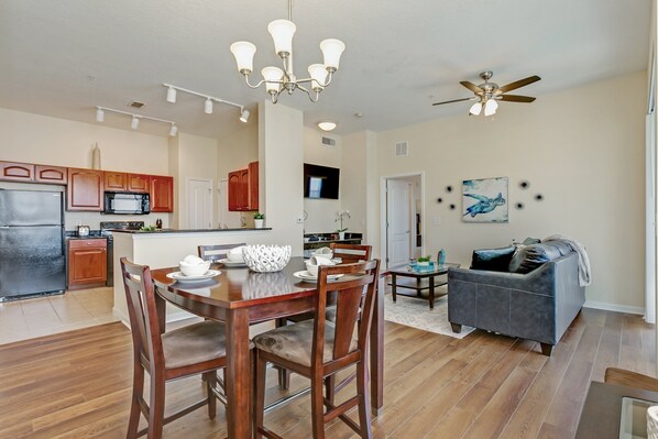 A spacious kitchen with wooden cabinets, a dining table with chairs, a ceiling fan, and a living area with a sofa and a TV.