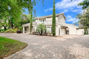 A two-story house with a balcony, surrounded by a well-maintained garden and tall trees. - Ultimate 6 Bedroom 5 Bathroom On Bay Hill (Orlando)