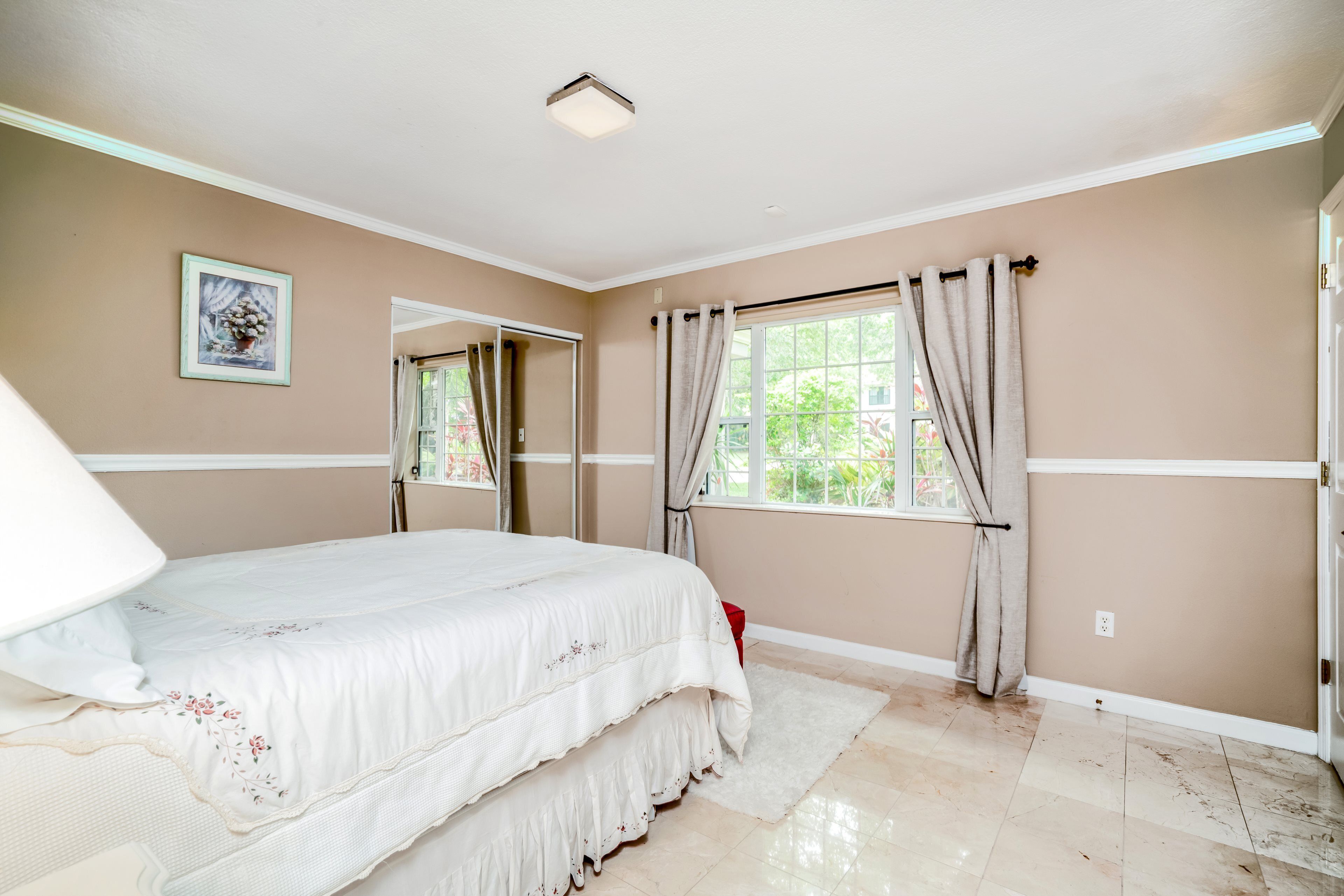 A bedroom with a bed, a window with curtains, a mirror, and a wall-mounted picture.