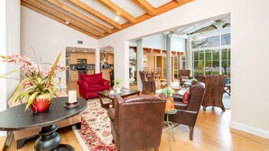 Un vaste espace de vie doté d’un plafond haut, de poutres en bois, d’un canapé rouge, de fauteuils en cuir, d’une table à manger et offrant une vue dégagée grâce à de grandes fenêtres.