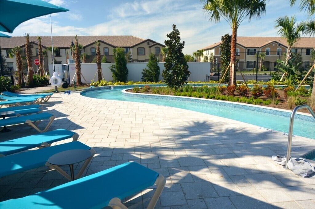 A pool area with lounge chairs, a pool, and a building in the background.