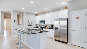 A modern kitchen with white cabinets, stainless steel appliances, and a central island with bar stools. - 2142victoria (Davenport)