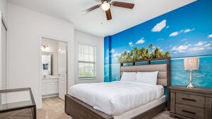 A bedroom with a bed, a nightstand, a ceiling fan, a window with blinds, and a wall mural of a tropical beach scene.