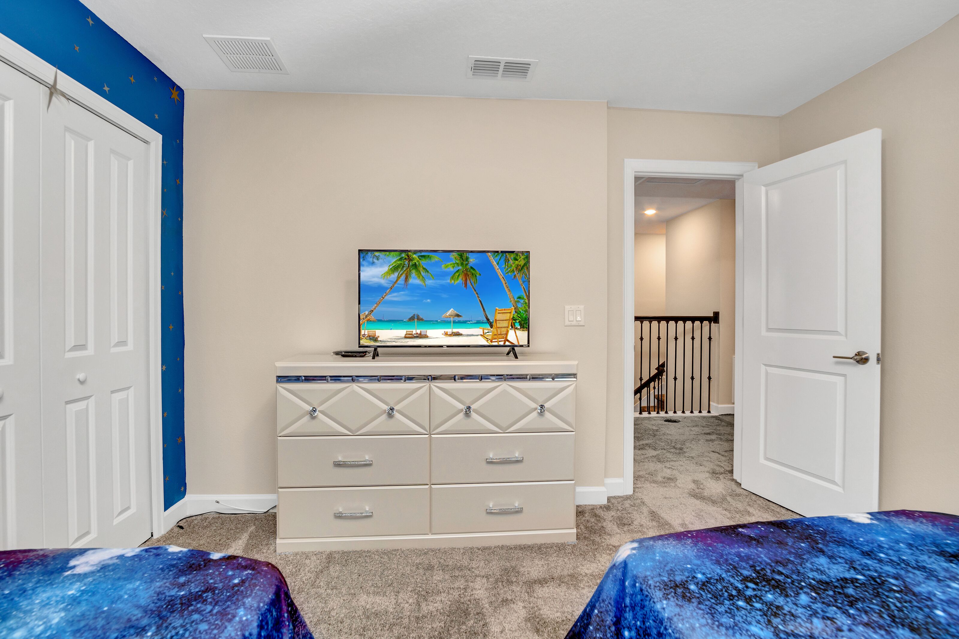 A bedroom with a bed, dresser, and a TV on a dresser displaying a beach scene.