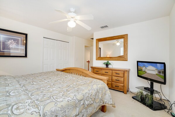 Un dormitorio con cama, cómoda, televisor y ventilador de techo.