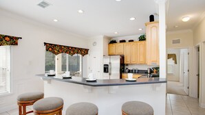 Cozinha moderna com ilha central, banquetas de madeira e uma janela grande com cortina decorativa.