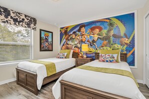 Une chambre avec deux lits, une grande fresque murale représentant des personnages de dessins animés et une fenêtre avec des stores.