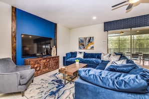 Un salon moderne avec un mur d’accent bleu, un grand téléviseur à écran plat, un canapé d’angle, une table basse et un tapis à motifs.