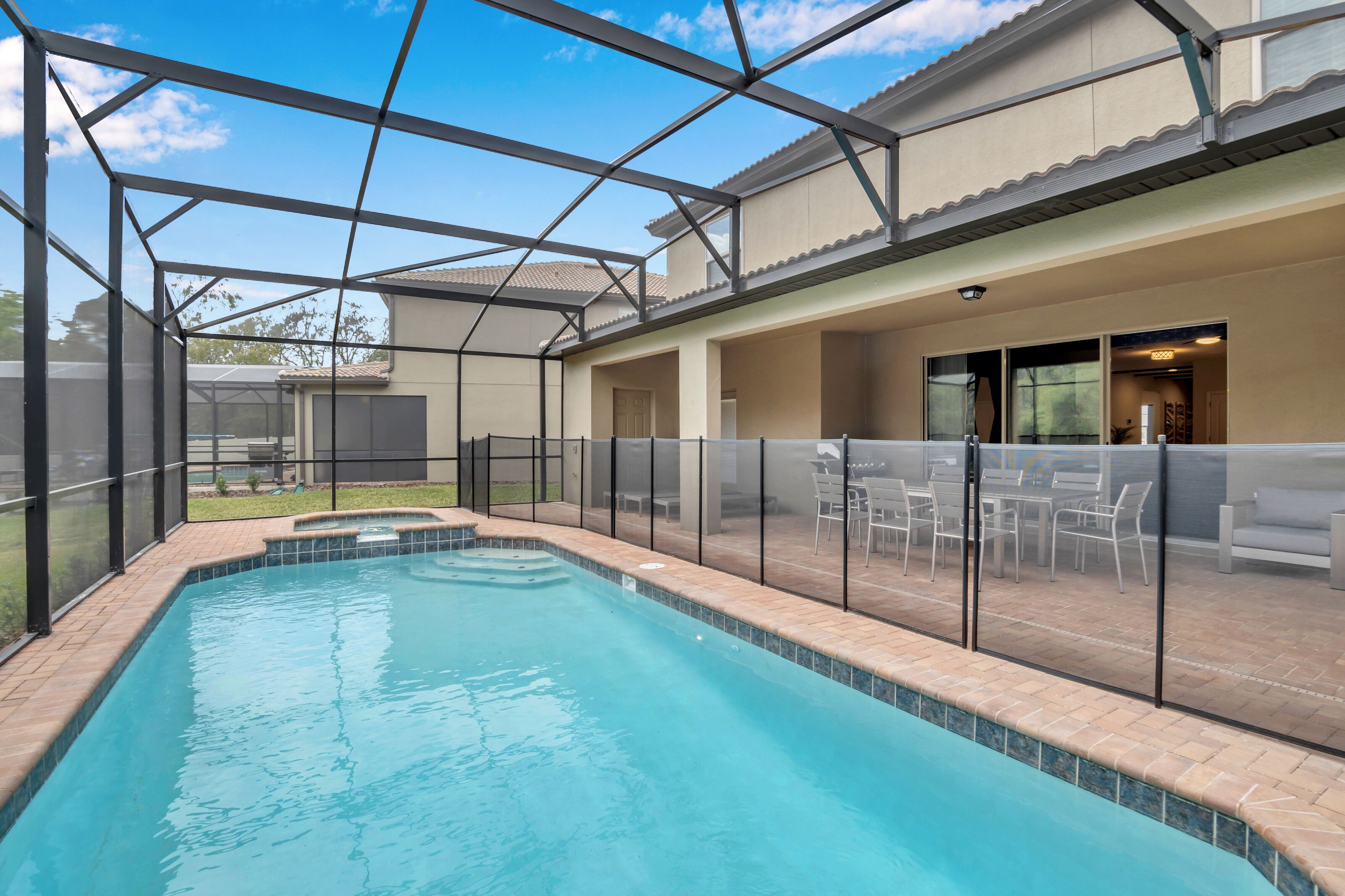 An indoor swimming pool with a glass enclosure, surrounded by a patio area with outdoor furniture.