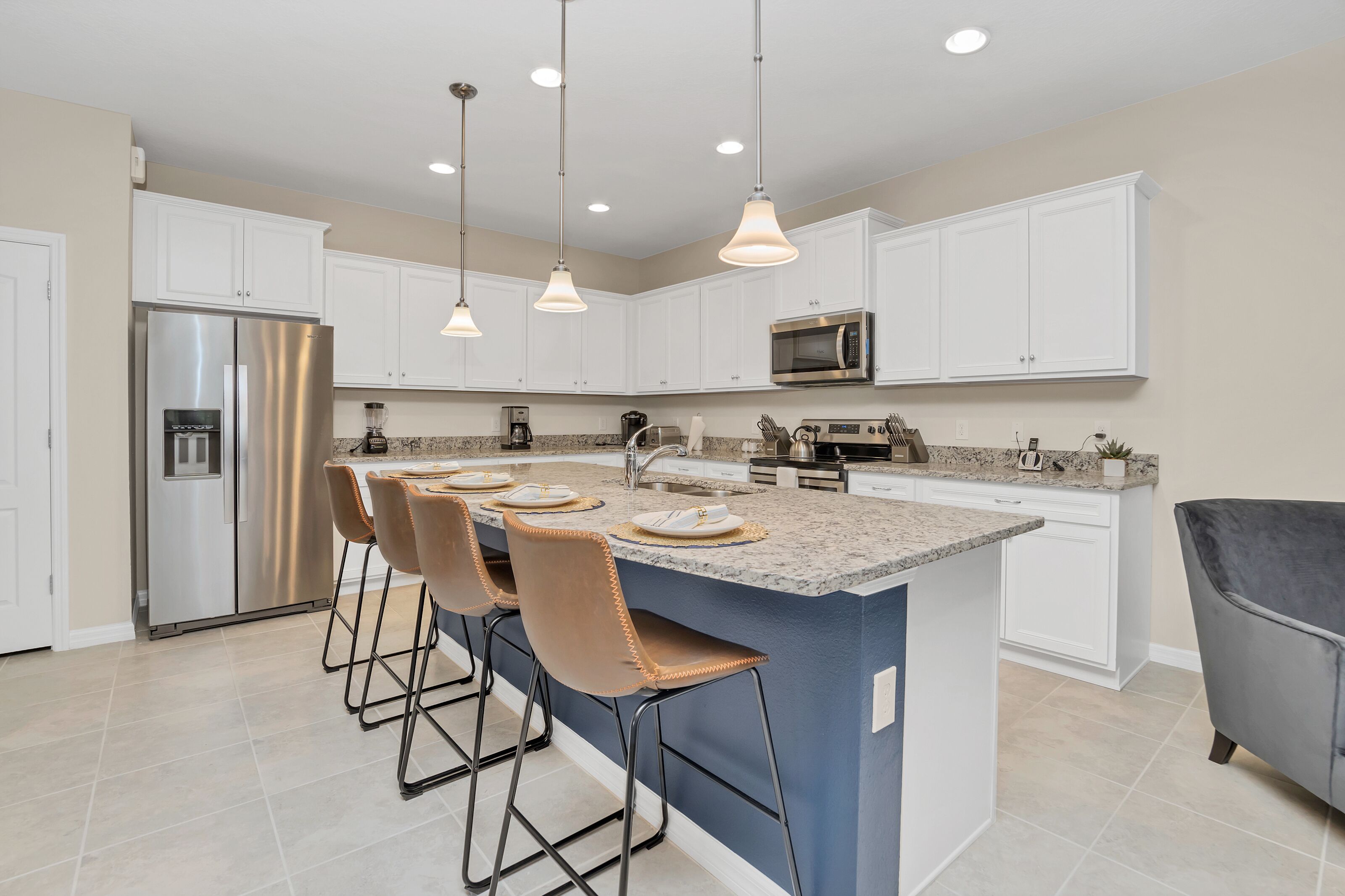 A modern kitchen with white cabinets, stainless steel appliances, a granite countertop, and pendant lighting.