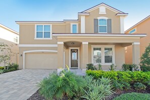 A two-story house with a beige exterior, a front garage, and a well-maintained garden with various plants.