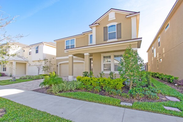 A residential building with a beige exterior, a front porch, and a well-maintained garden.
