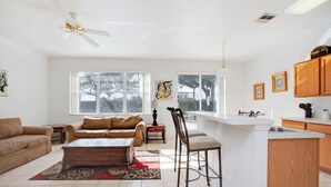 A spacious living room with a sofa, coffee table, and a dining area with chairs and a kitchen island. - 1418pine (Davenport)