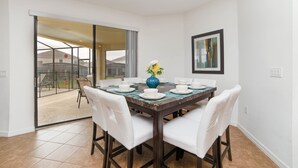 A dining area with a table set for four, white chairs, a vase with flowers, and a sliding glass door leading to a patio. - 2629rose (Davenport)