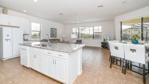 A spacious kitchen with white cabinets, a granite countertop, and a large island. There is a dining area with a table and chairs, and a window providing a view of the outside. - 2629rose (Davenport)