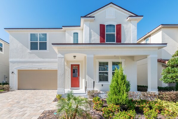 Une maison à deux étages avec une porte rouge, une façade blanche et un garage.