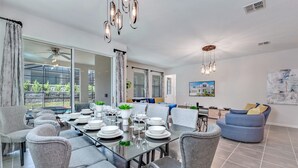 A modern dining area with a glass table set for six, grey upholstered chairs, and pendant lighting.