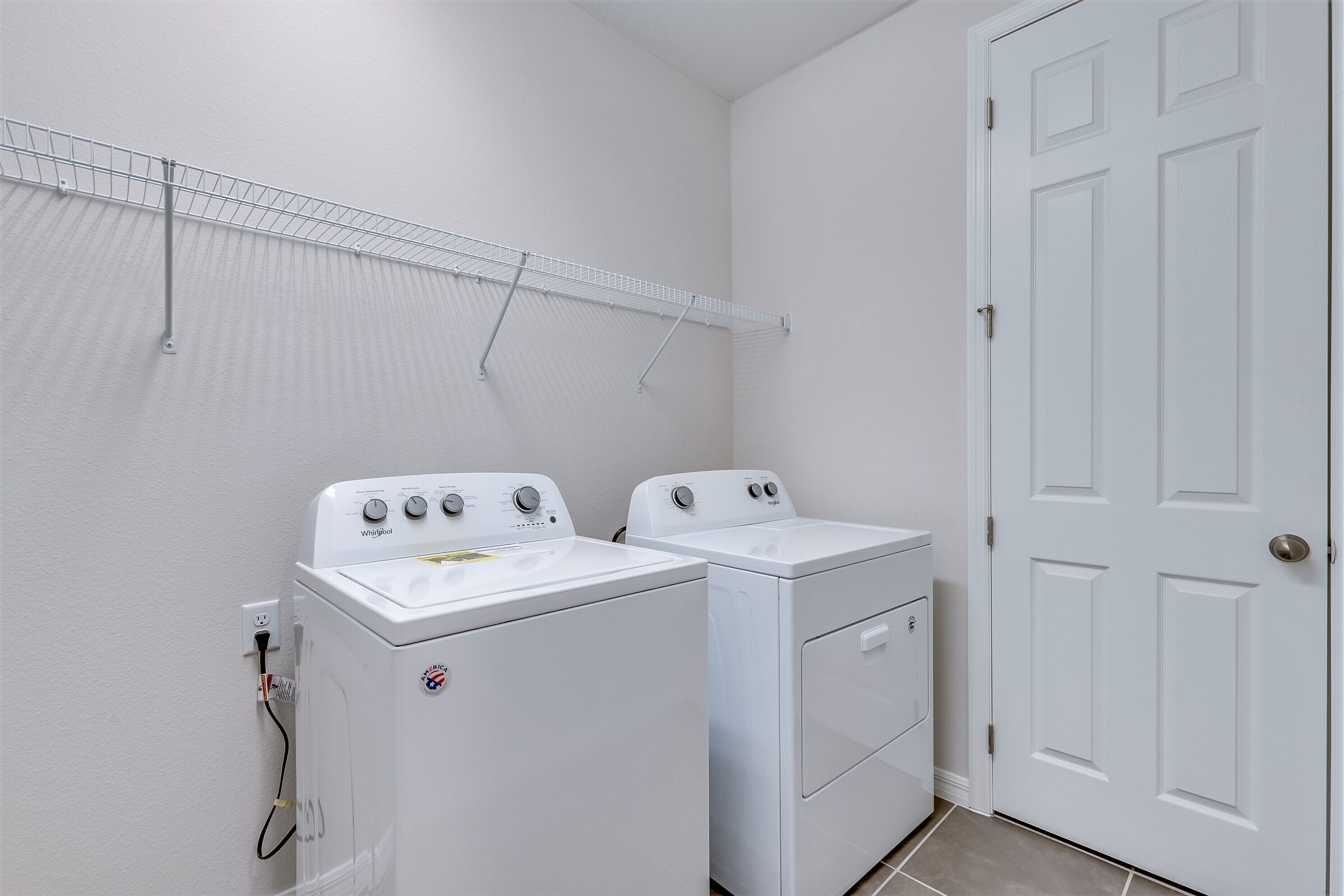 A laundry room with two white front-loading washers and dryers, a metal drying rack, and a white door.
