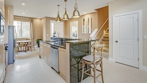A modern kitchen with a central island, pendant lighting, and a staircase leading to an upper level. - Modern Magic Village Resort Townhome (Kissimmee)