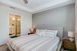 Une chambre à coucher comprenant un lit, des tables de chevet, un miroir et une porte donnant sur une salle de bain.