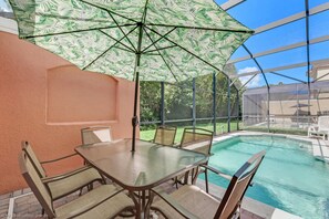 Un espace piscine intérieur avec une table et des chaises en verre, un grand parasol et une vue sur le jardin extérieur.