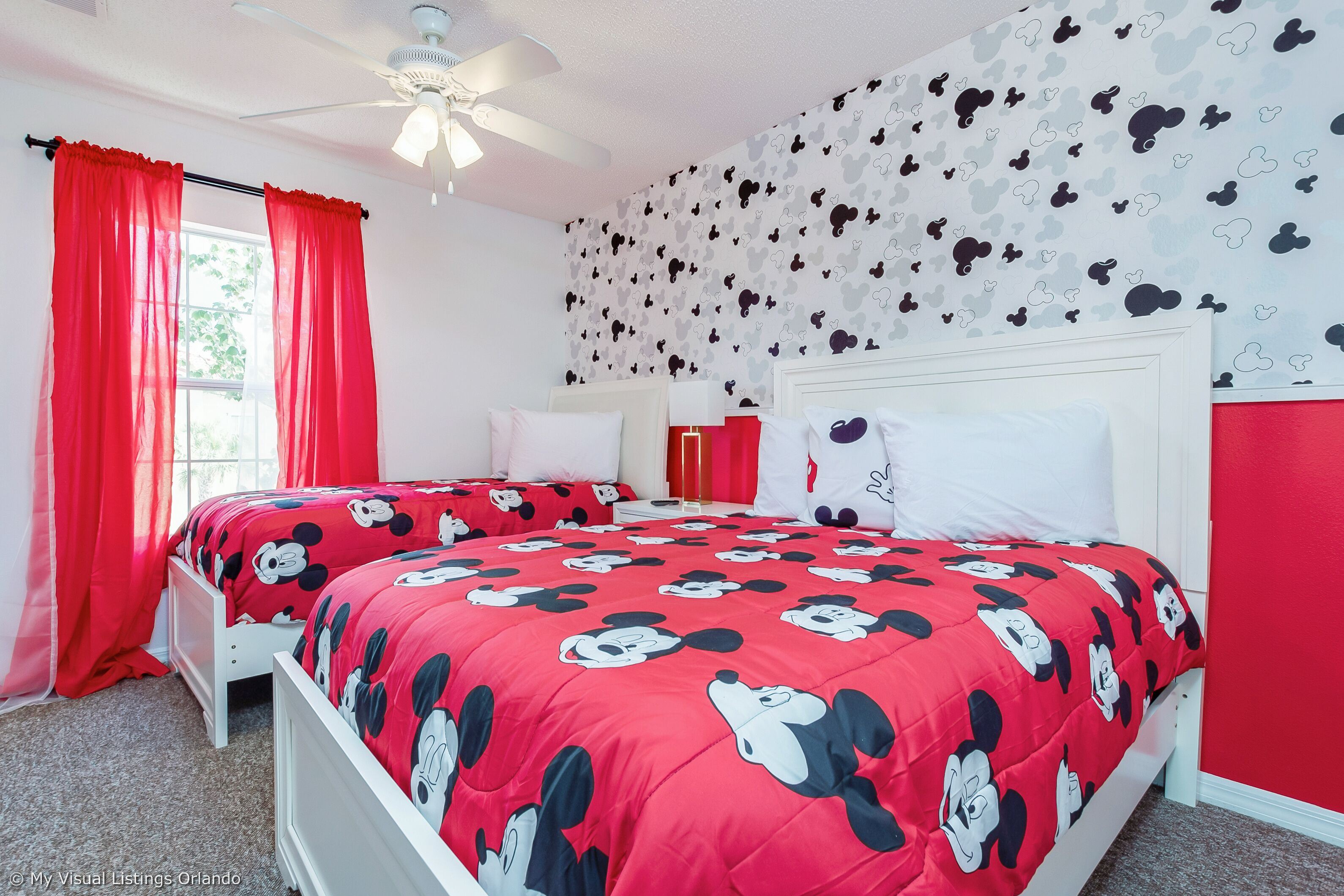 Een slaapkamer met een bed bekleed met rode beddengoed met cartoonfiguren, een wit hoofdeinde en een plafondventilator.
