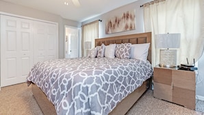 A bedroom with a large bed, a nightstand, a ceiling fan, and a door. - 4732tvero (Kissimmee)