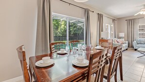 A dining area with a wooden table set for four, chairs, and a view of a garden through large windows. - 4732tvero (Kissimmee)