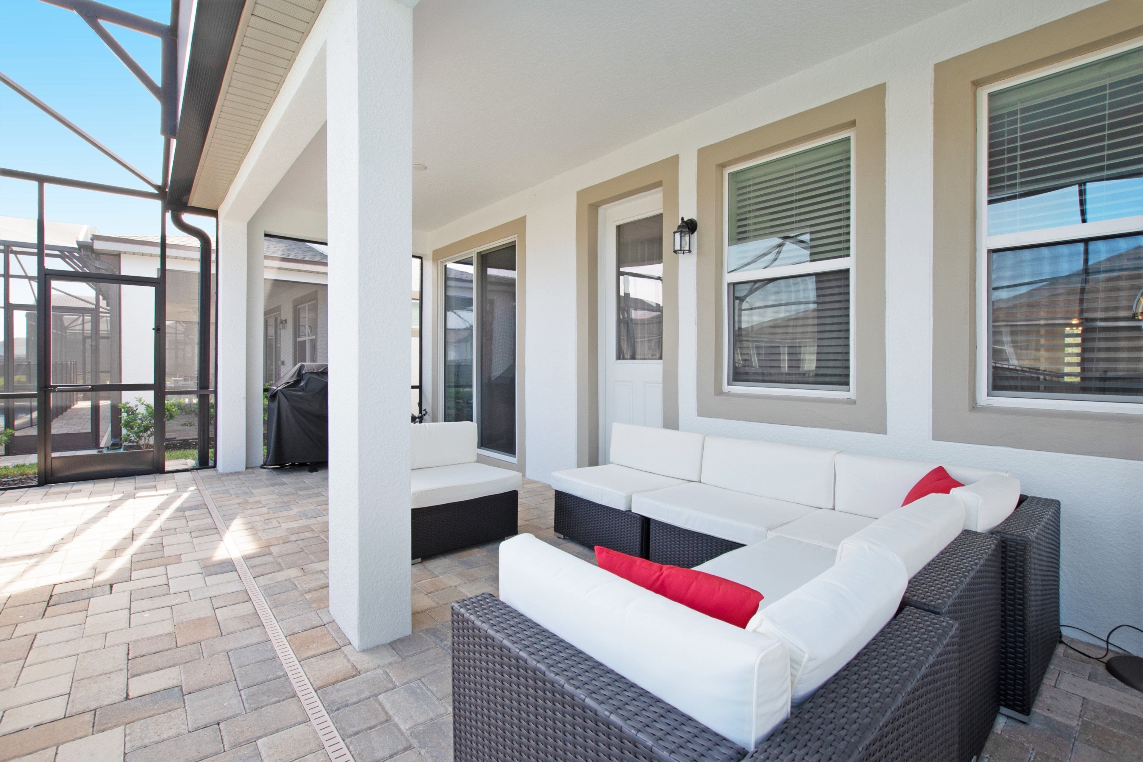 A covered patio area with outdoor seating, including a sofa and a bench, and a grill.