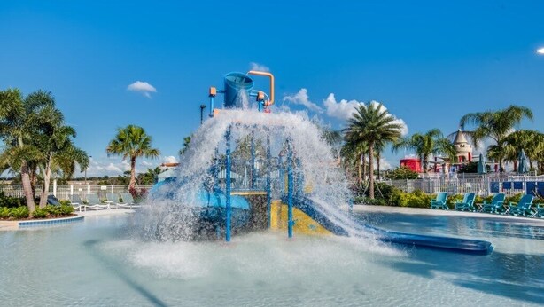 A water park with a central water feature, surrounded by palm trees and a clear blue sky.