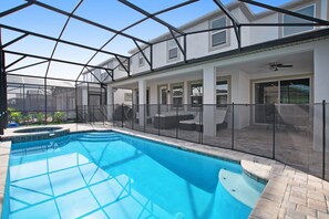 A swimming pool with a glass enclosure, a covered patio area with outdoor furniture, and a ceiling fan. - 1823carri (Kissimmee)
