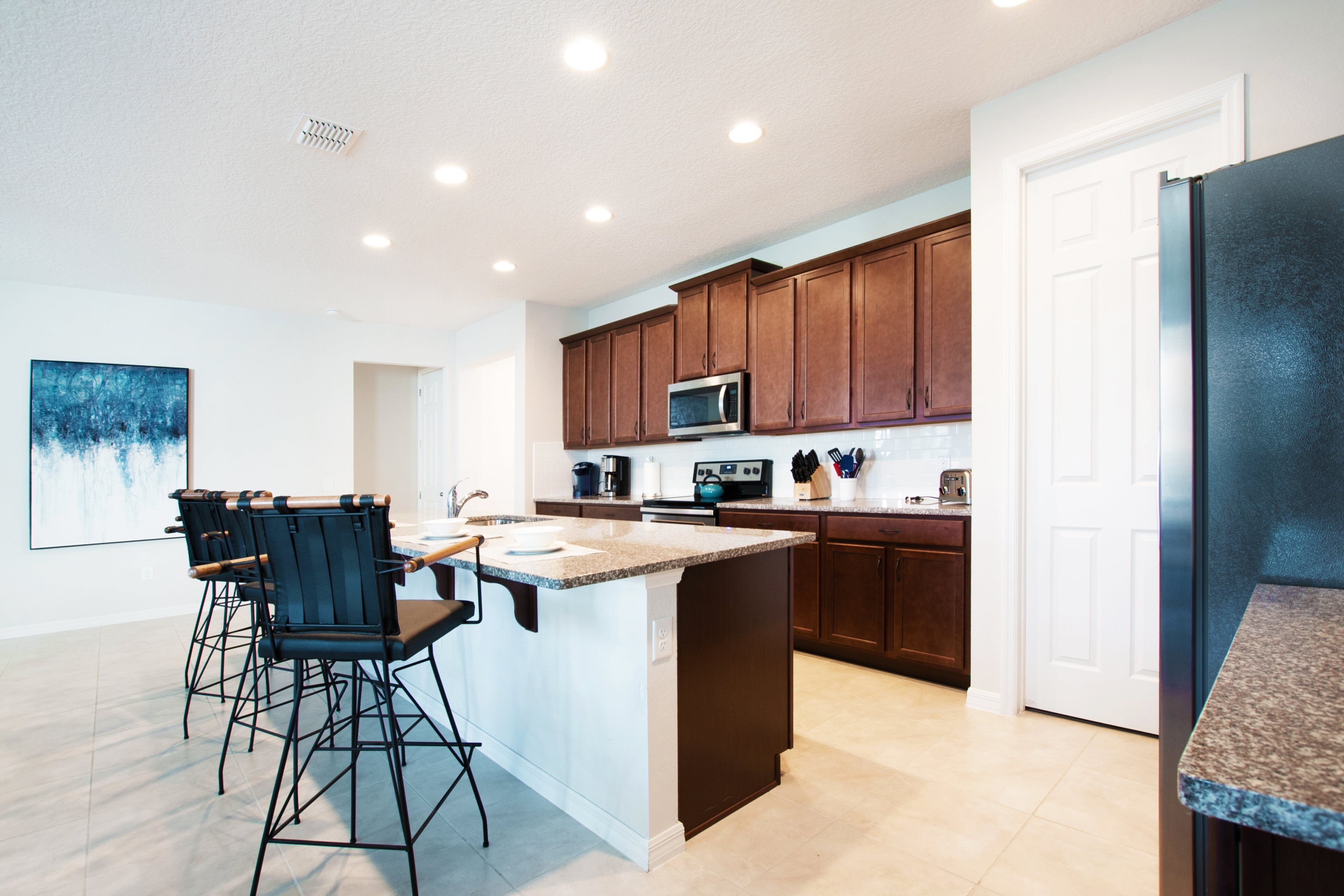 A modern kitchen with dark wooden cabinets, a granite countertop, and a central island with bar stools.