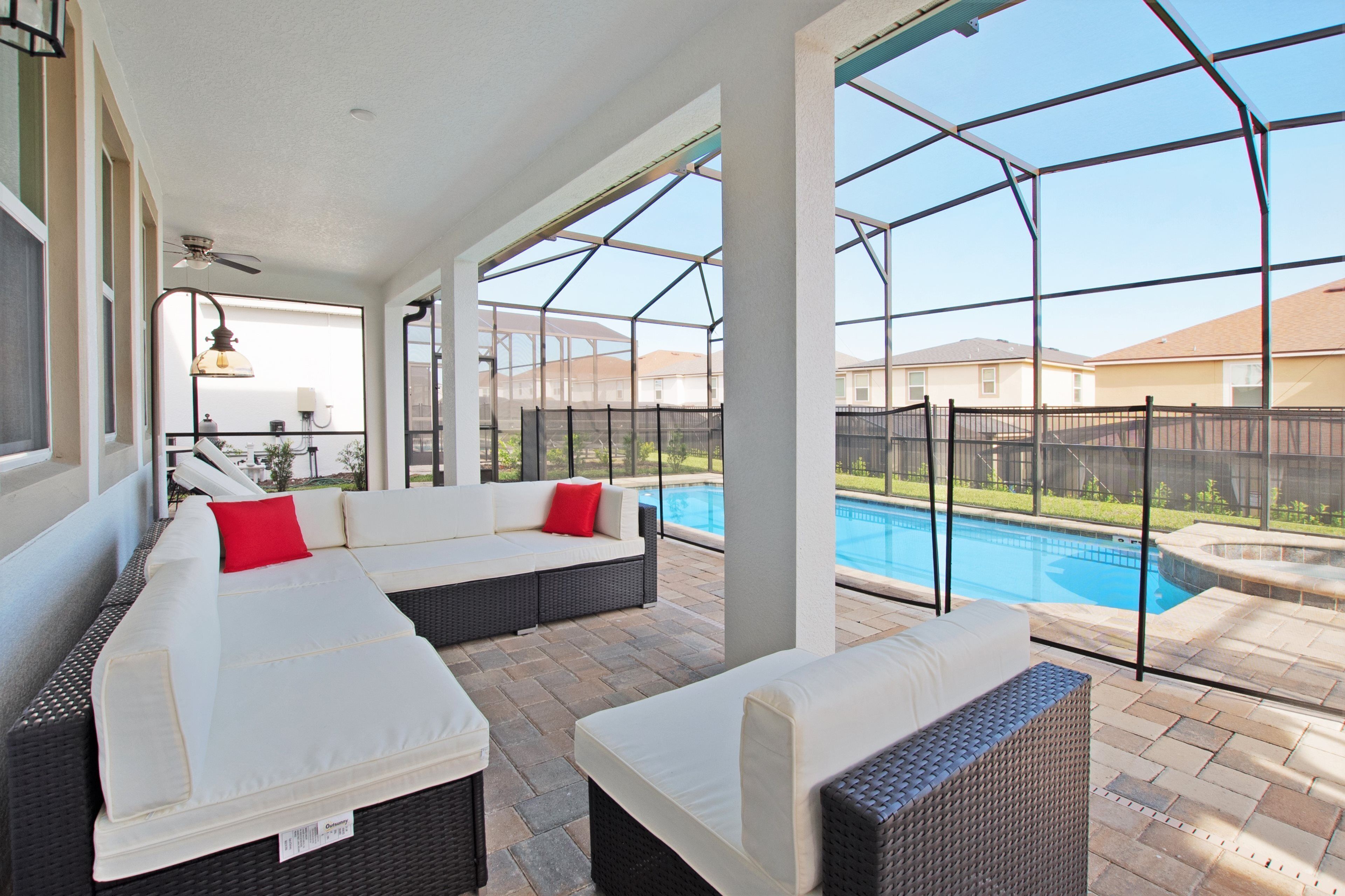 A covered patio area with two wicker sofas, a ceiling fan, and a view of a swimming pool.