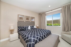 A bedroom with a large bed, a bedside table, a lamp, and a window with curtains.