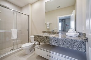 A modern bathroom with a glass shower enclosure, a white toilet, a granite countertop, and a large mirror.
