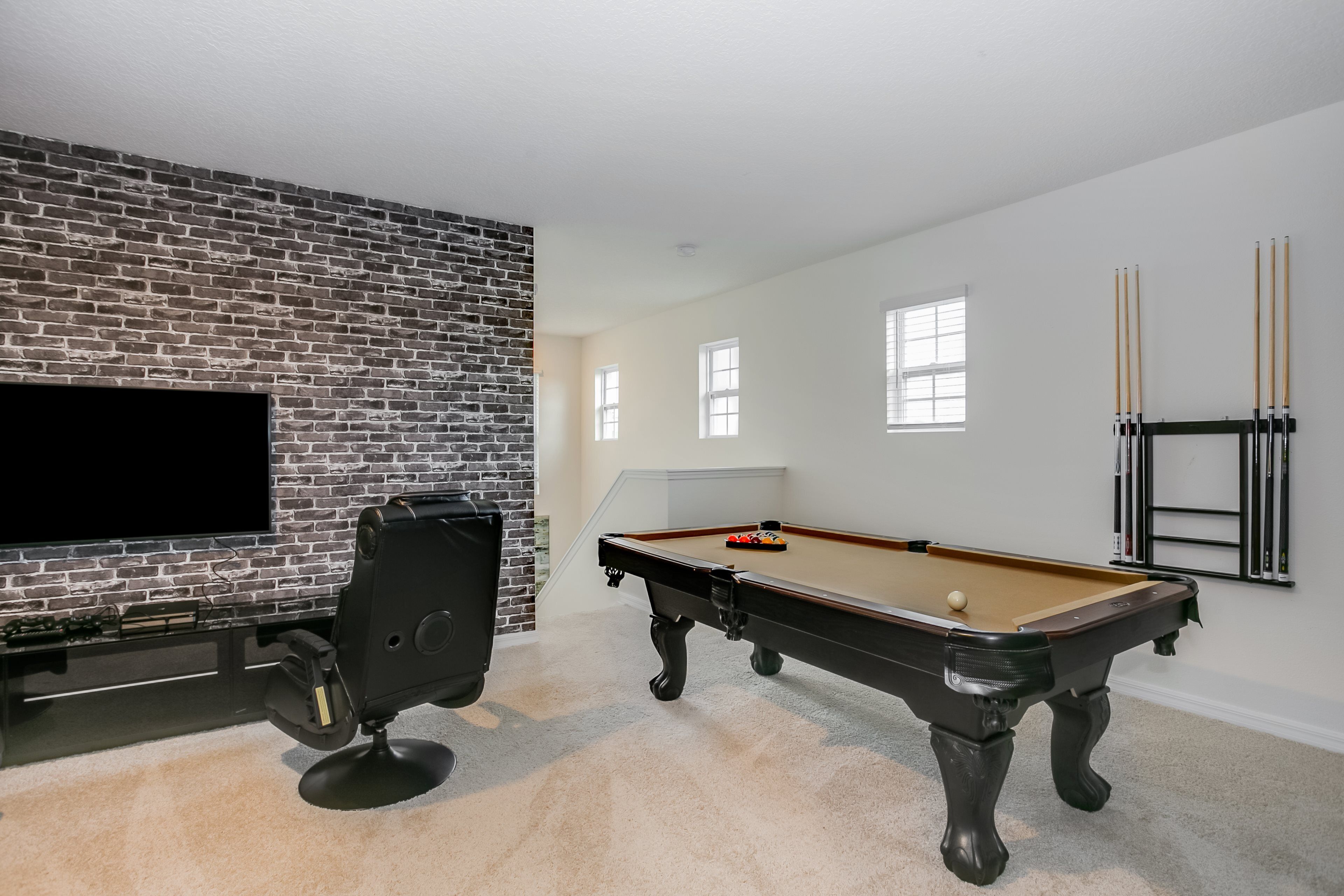 Une pièce équipée d’une table de billard, d’un téléviseur à écran plat fixé à un mur en briques, d’un fauteuil confortable et d’un porte-tailles.