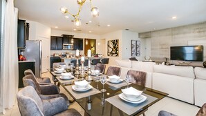 A modern dining area with a glass table, grey upholstered chairs, and a chandelier. - 6bed 4Ba Villa Game Room Pool Spa (Davenport)